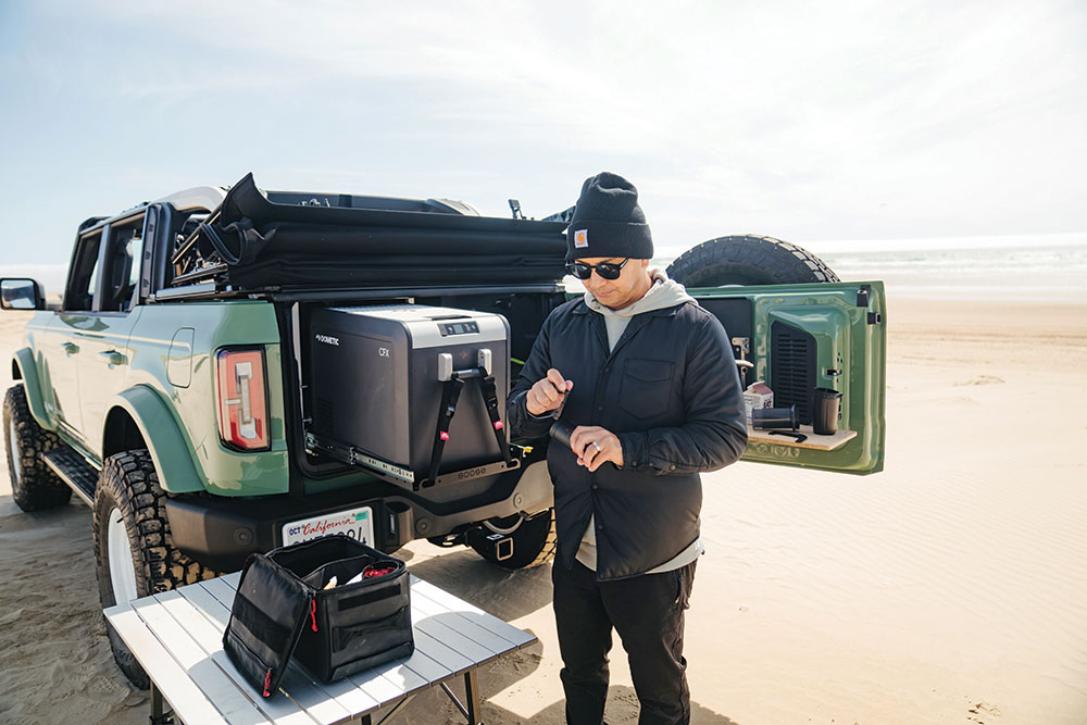 Pangilinan, in a hoodie and hat, pulls the fridge out of the back of the Bronco.