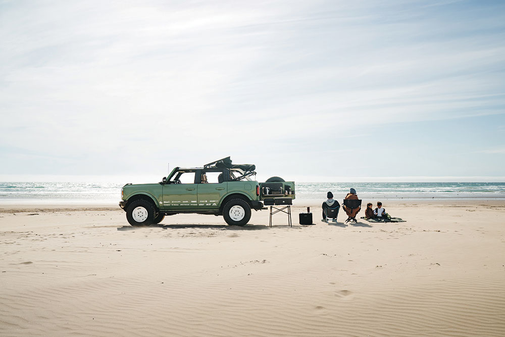 The Pangilinan family sits on the beach next to the green '22 Ford Bronco.