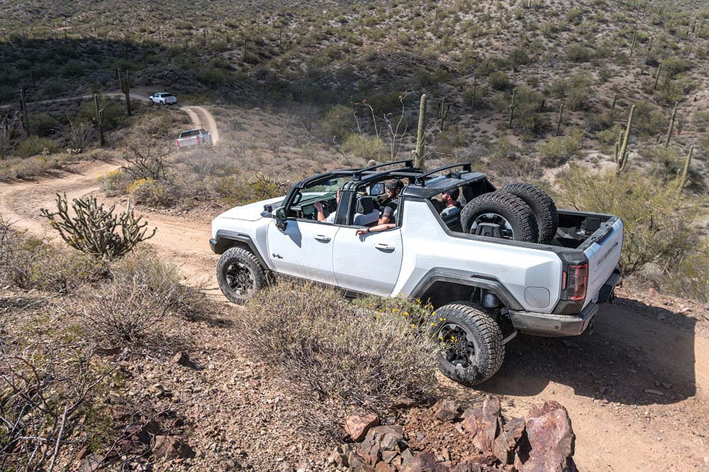 People ride down a dirt trail in the white truck with the top off.