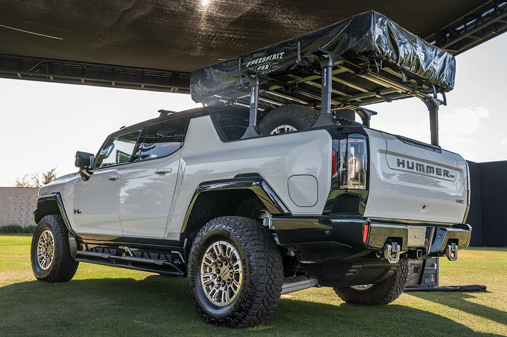 The Hummer parks on grass with a roof top tent over the bed.