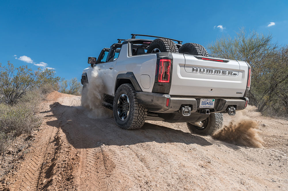 The truck kicks up dust as it drives over a gravel path in the desert.