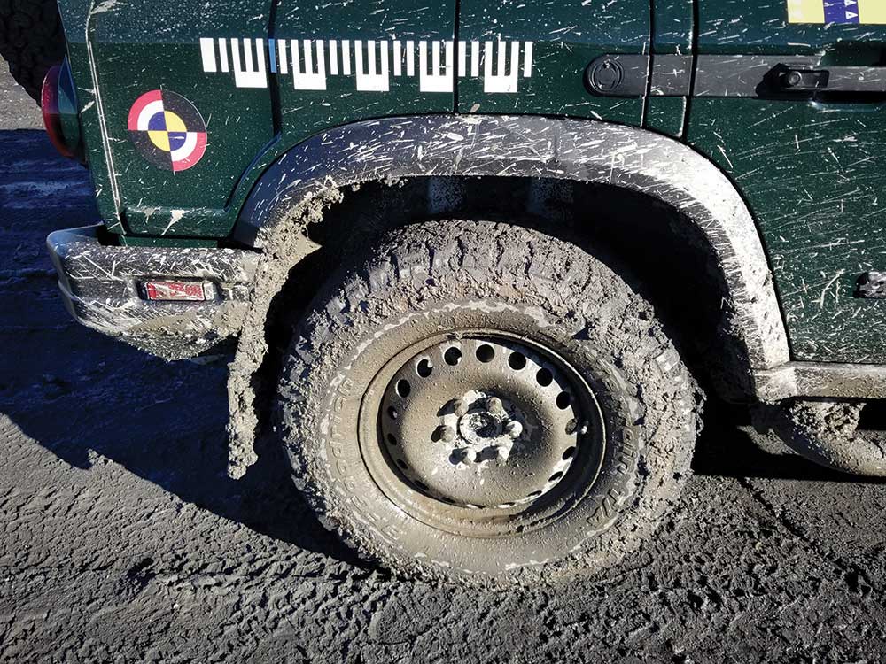 The rear tire of a green vehicle is caked in mud.