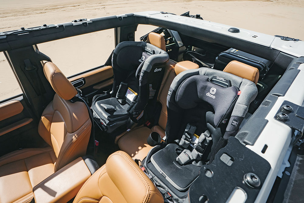 The open top of the Bronco reveals tan leather interiors with two black car seats in the back.