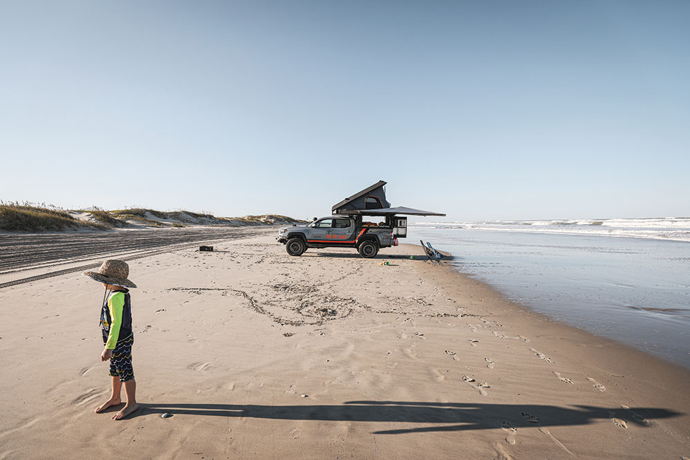 Truck is set up on the beach with a child in the foreground. 