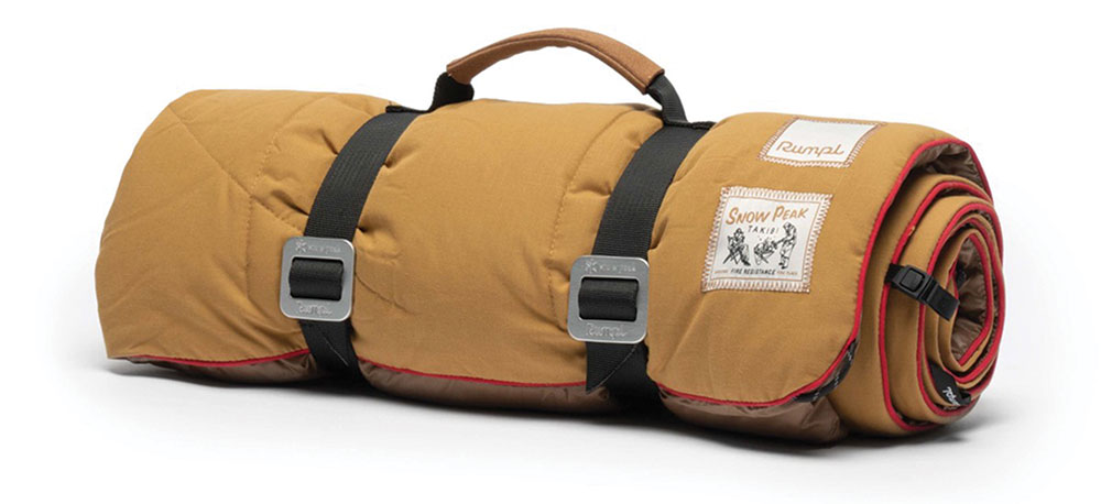 A rolled up light brown blanket with red stitching is secured with straps and a handle.