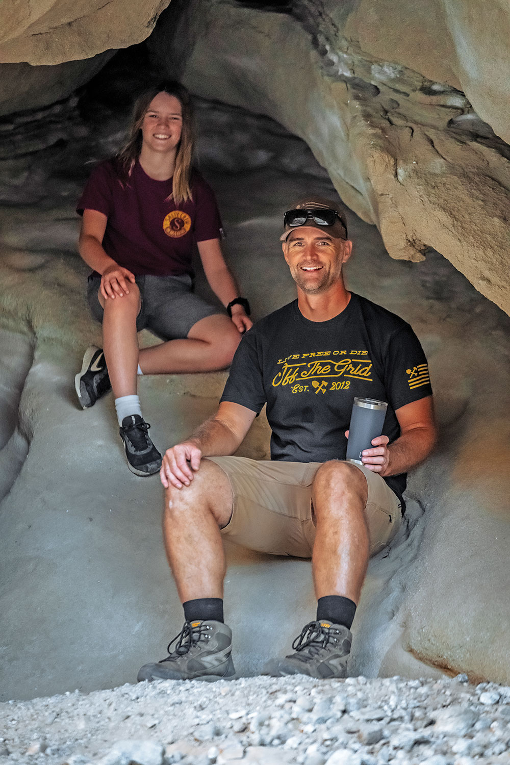 Dean and his daughter sit in a rocky cave.