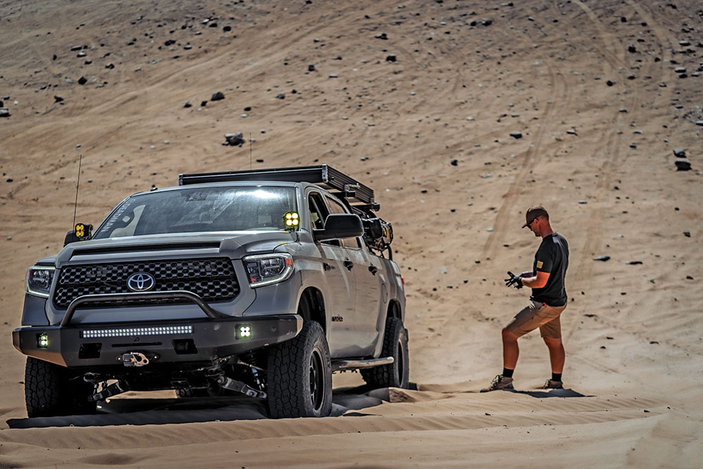 Samuel stands on the sand next to the Tundra.