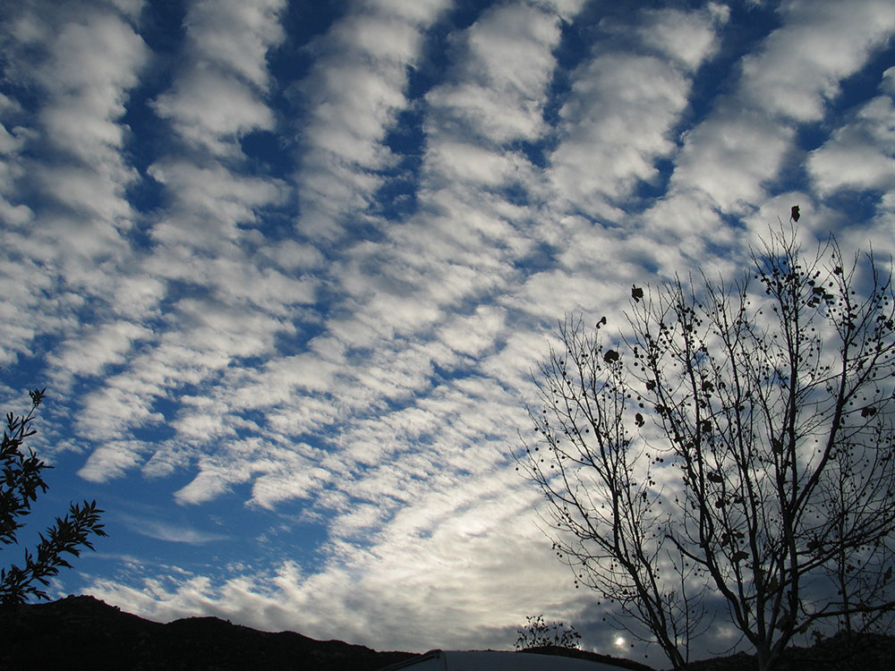 Lumpy lines of clouds only partially block out the blue sky.