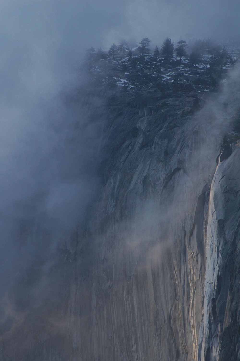 A thin layer of clouds drapes over a rocky cliff face.