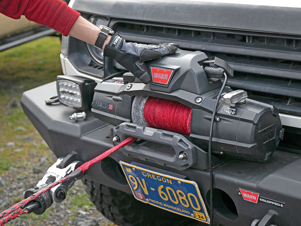 A gloved hand supports the electric winch on the front of this truck as it winds in.