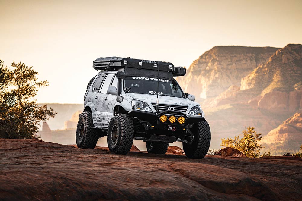 The white SUV with large tires and roof top storage parks on a cliff edge.