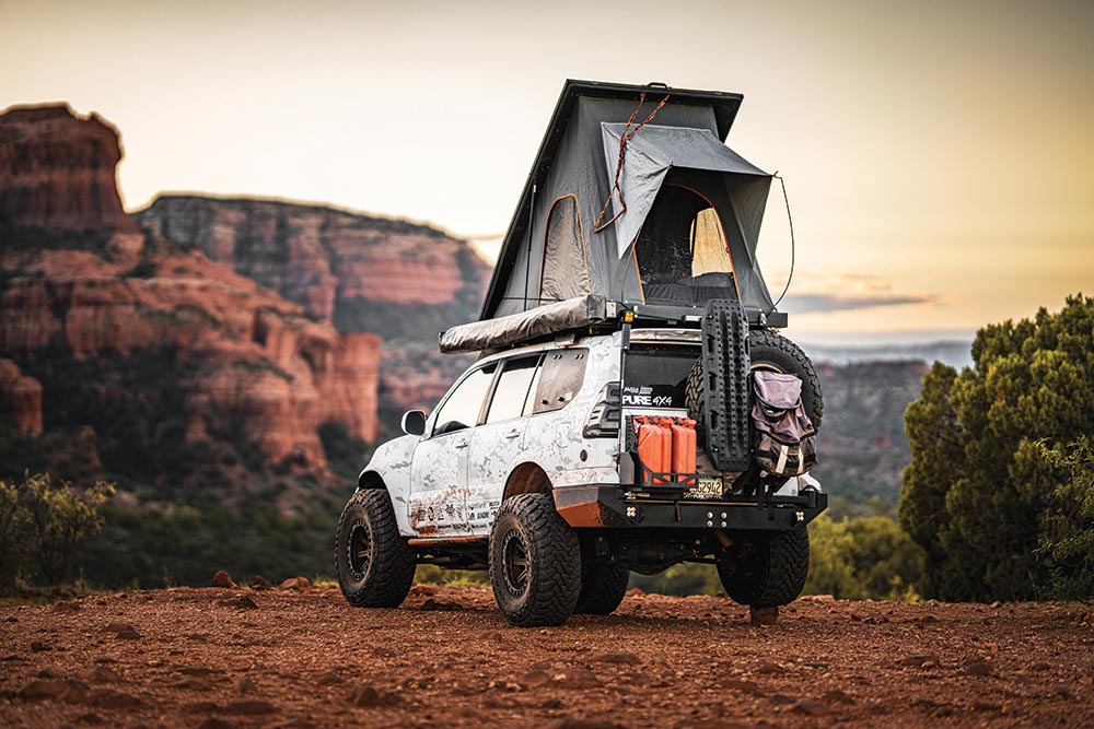 The white SUV parks on the edge of a cliff with the roof top tent up.