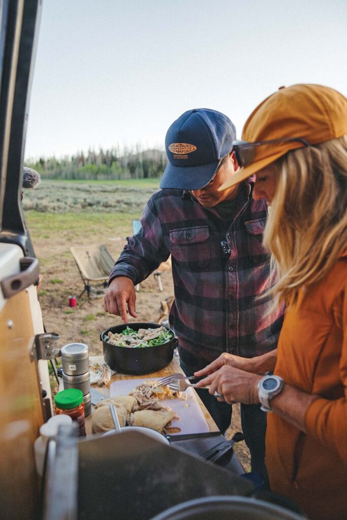 A man and a woman cooking on the tailgate of the Troopy while traveling.