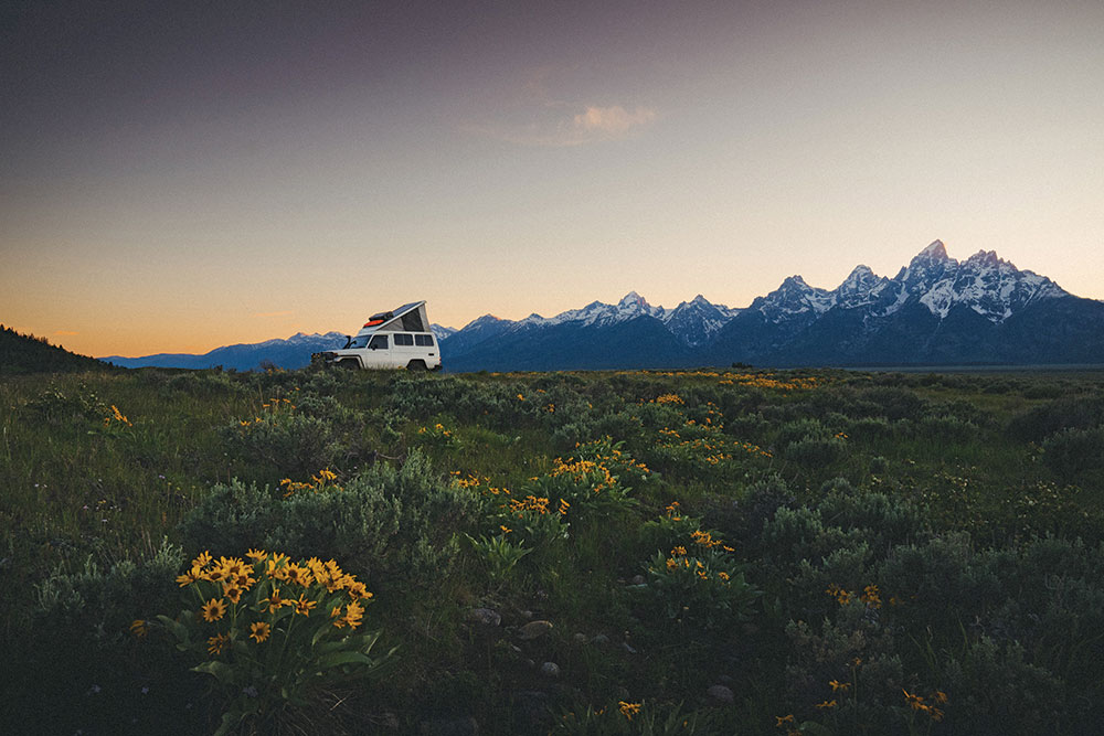 The Troopy with top popped up parks in front of a beautiful sunset view while traveling in the Grand Tetons.