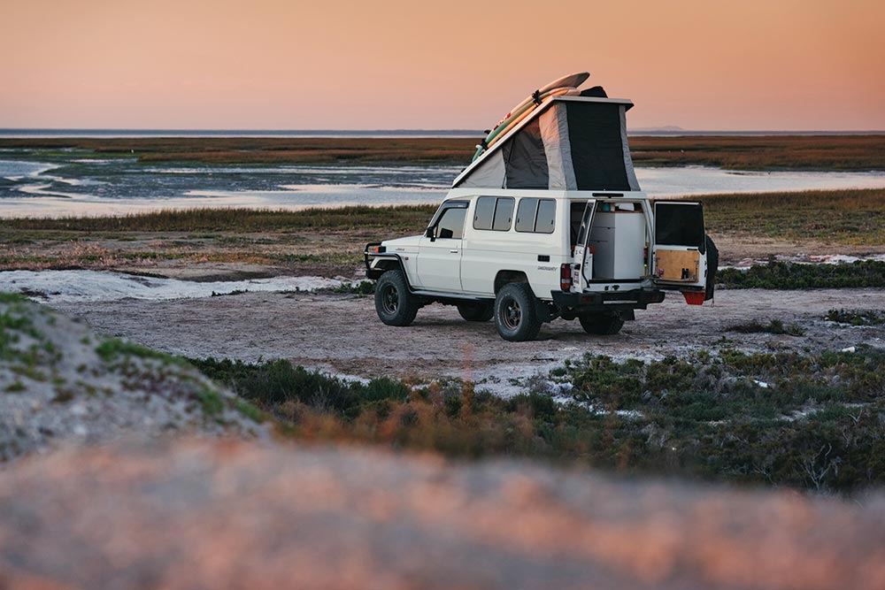 The SUV parks with the top up and rear door open on the beach while traveling at sunset in Mexico.