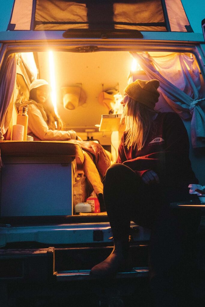 Two women sit in the back of the Troopy, illuminated by yellow light.