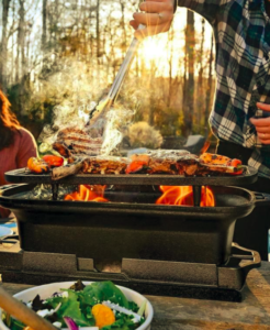 A man flips chicken as flames emerge from the bottom of this camp grill.