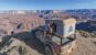 Man sits on edge of rooftop tent on top of Jeep Gladiator and enjoys a drink while looking out at the Grand Canyon.