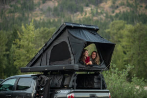 Two girls sit in a roof top tent while overlanding.