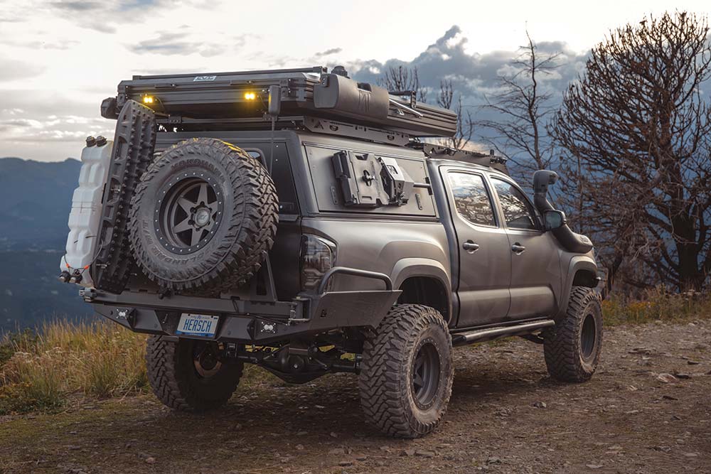 The black wrapped Tacoma features a large black steel rear bumper and roof top accessories.