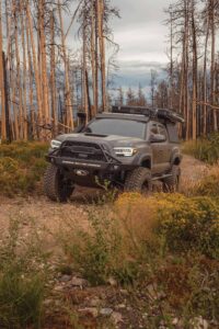 The HerschX Tacoma rolls through high grass. Its dark paint job stands out against the trail.