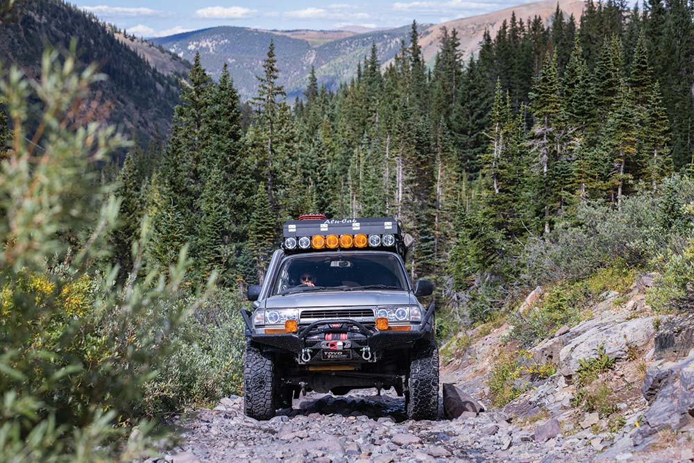 Climbing uphill from a background of tall pines, a head on look at the Land Cruiser's front grille.