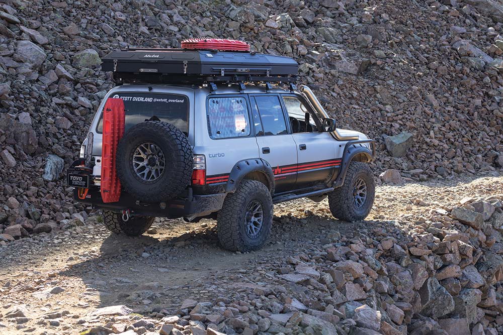 A rear view of the Land Cruiser heading up a mountain trail reveals a large rear mounted spare and a set of Maxtrax.
