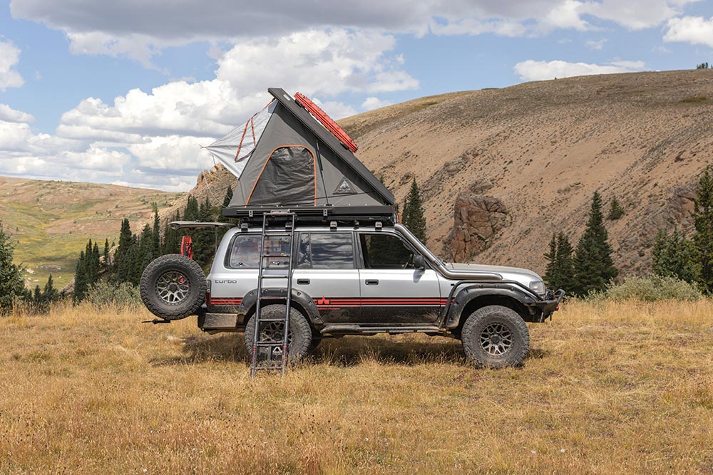 Parked in a grass field, the gray Land Crusier's roof top tent is deployed.