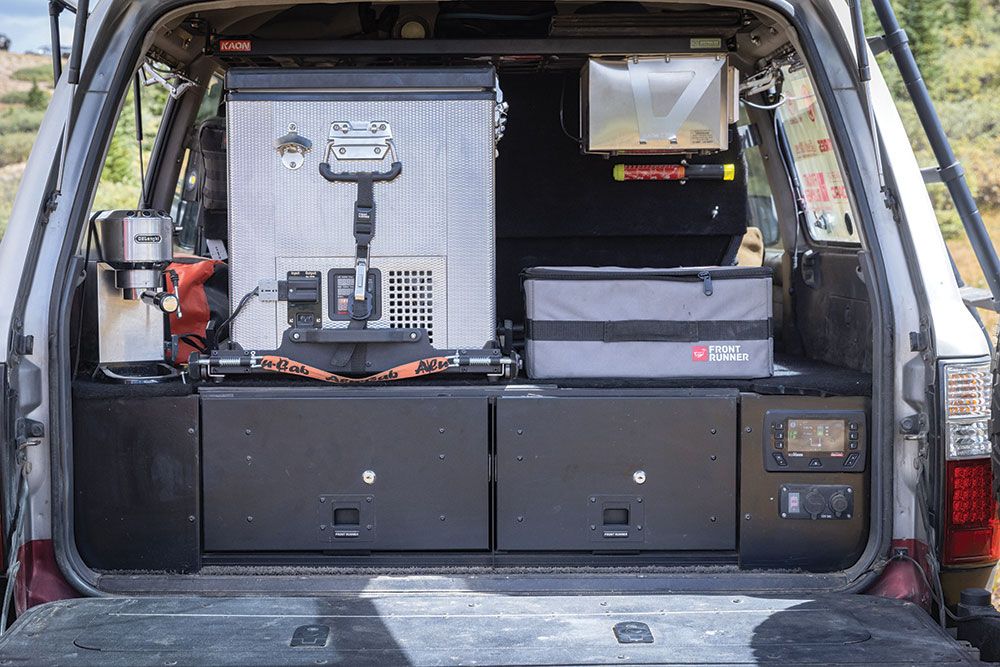 The view into the trunk includes custom drawers, a fridge, coffee machine, and storage space.