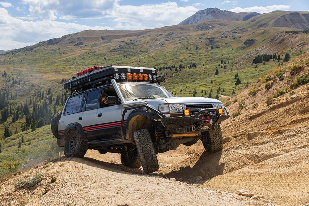 The Land Cruiser's suspension is hard at work as it drives over hilly terrain.