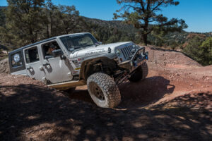 A Jeep Wrangler climbs uphill on off-road tires.