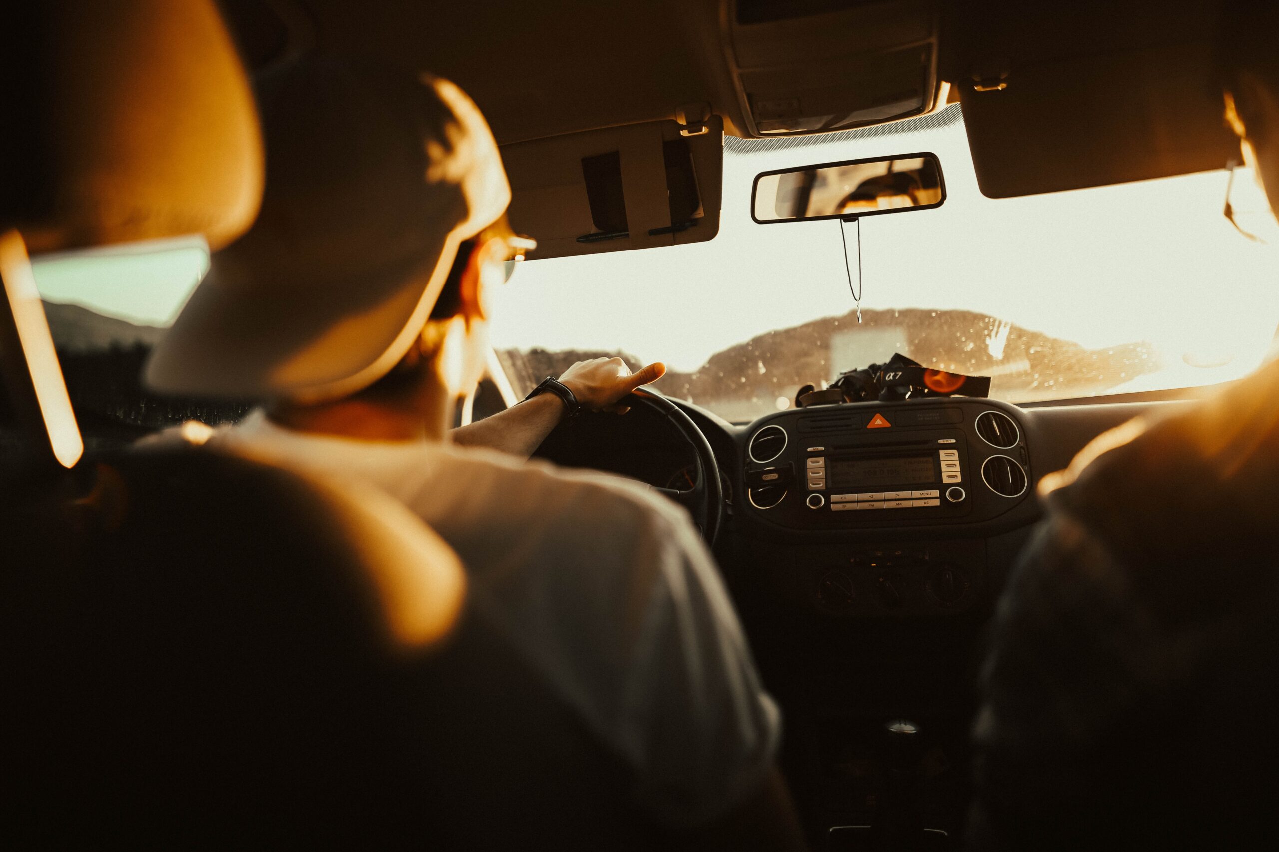 Man wearing backwards hat drives car with one hand while overlanding.