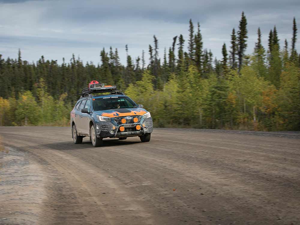 The orange and blue Subaru approaches from around a curve. 