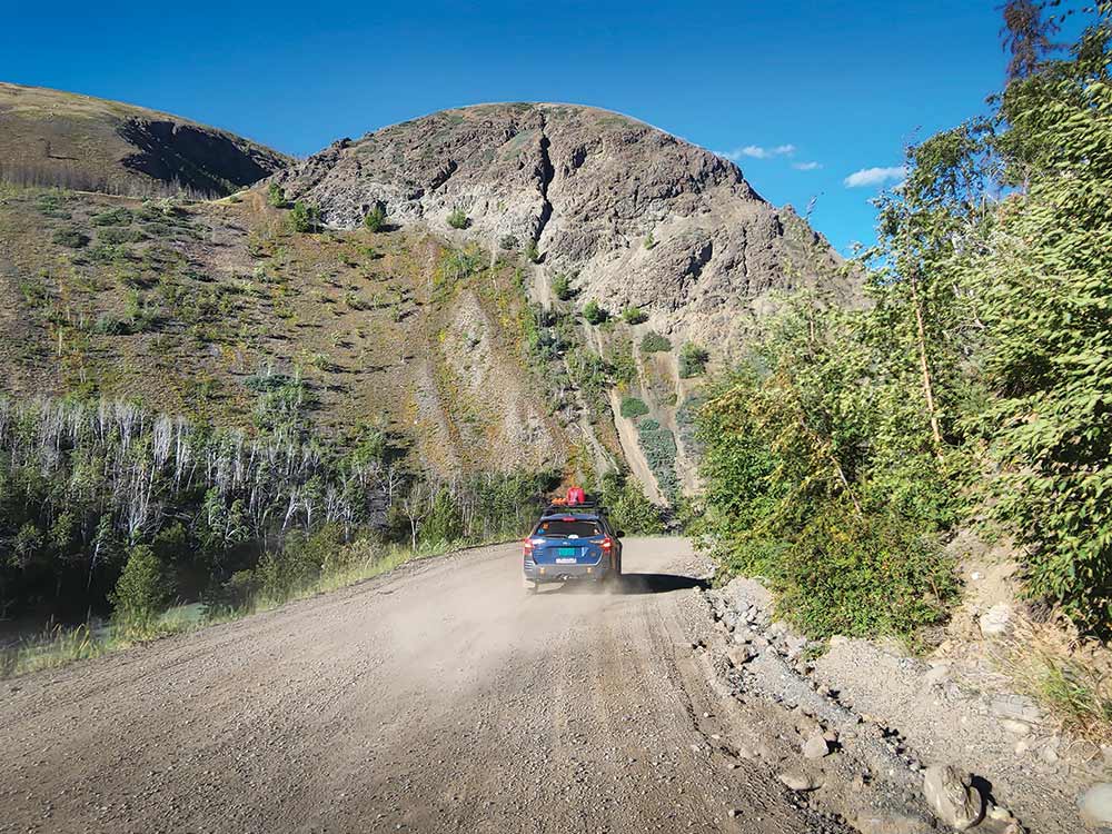 Driving away into a valley betwen two hills, the blue and orange Subaru kicks up dust.