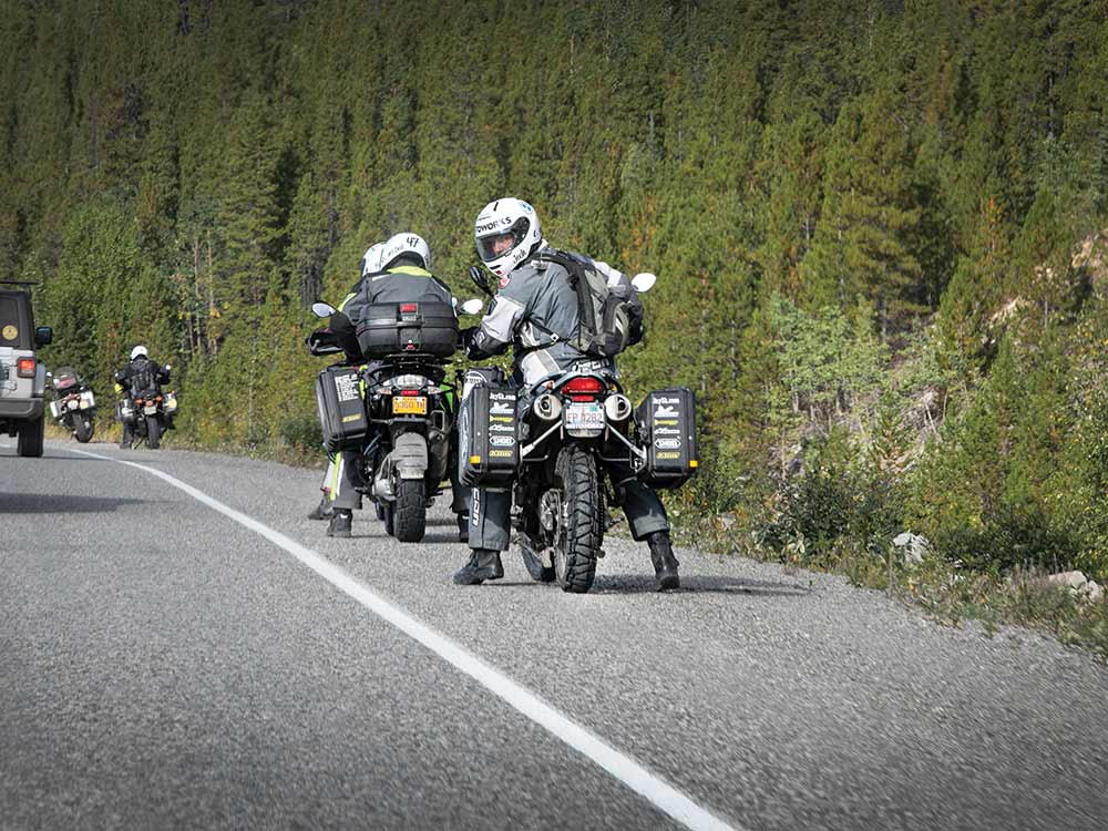 A pair of adventure motorcyclists pull over on the side of the road and check on the ralliers behind them.
