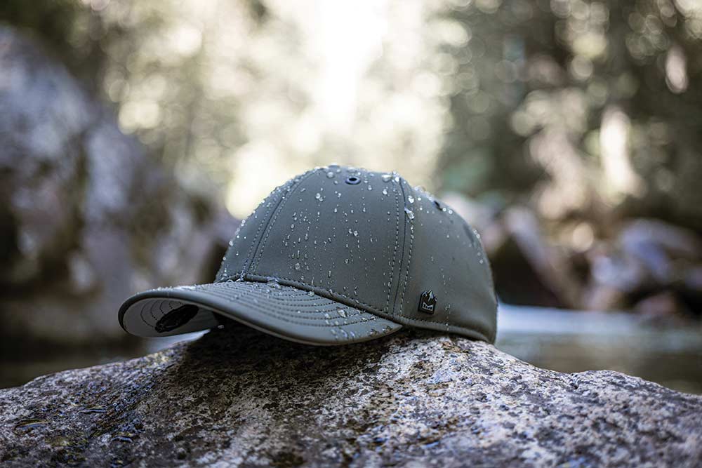 A green/gray ballcap splattered with some water droplets sits on a log.