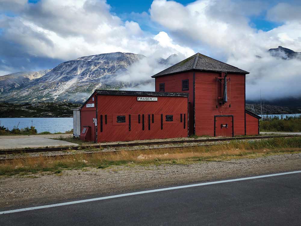 Nearby mountains and the red Fraser station building and waterhouse along the White Pass and Yukon Route.