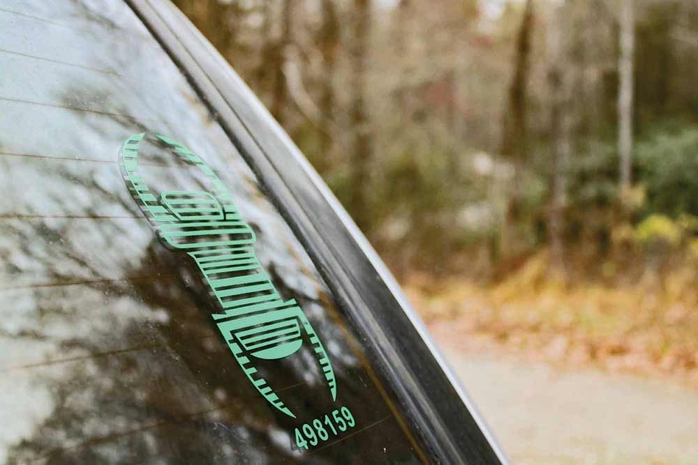 A decal of a trackable travel bug sticks on the back windshield of this van rig. Other cachers can log its location when spotted.