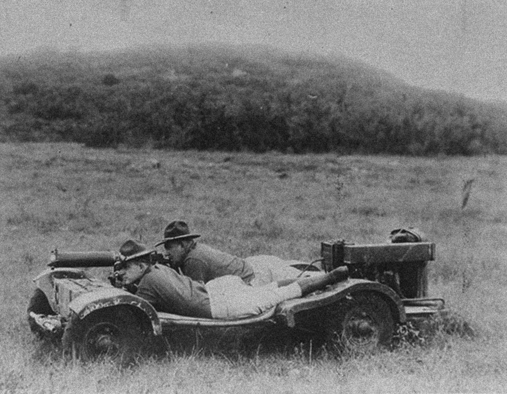 Two men lie prone on their stomachs on a flat platform with wheels, one of the earliest Jeep experiments before Karl Probst's invention.