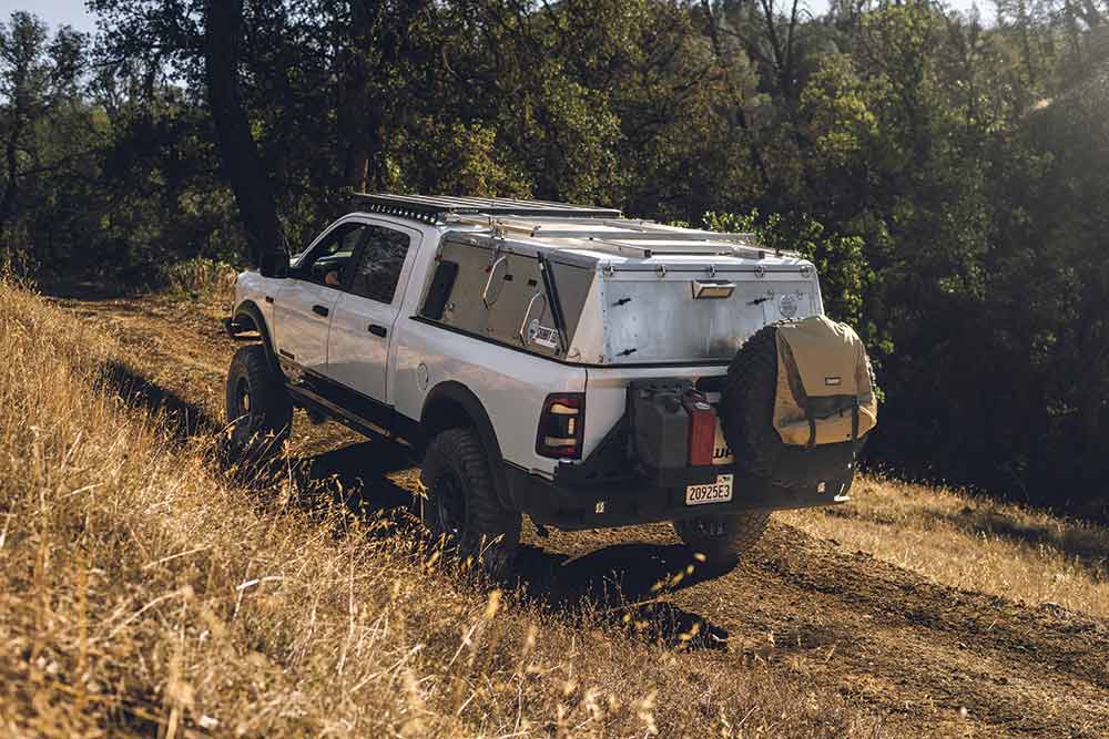 The white RAM 2500 truck with sliver topper drives up a grassy hill.