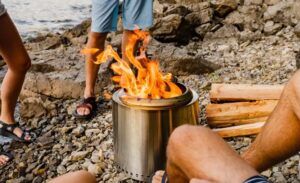 The metal cylinder holds a fire on a rocky beach.