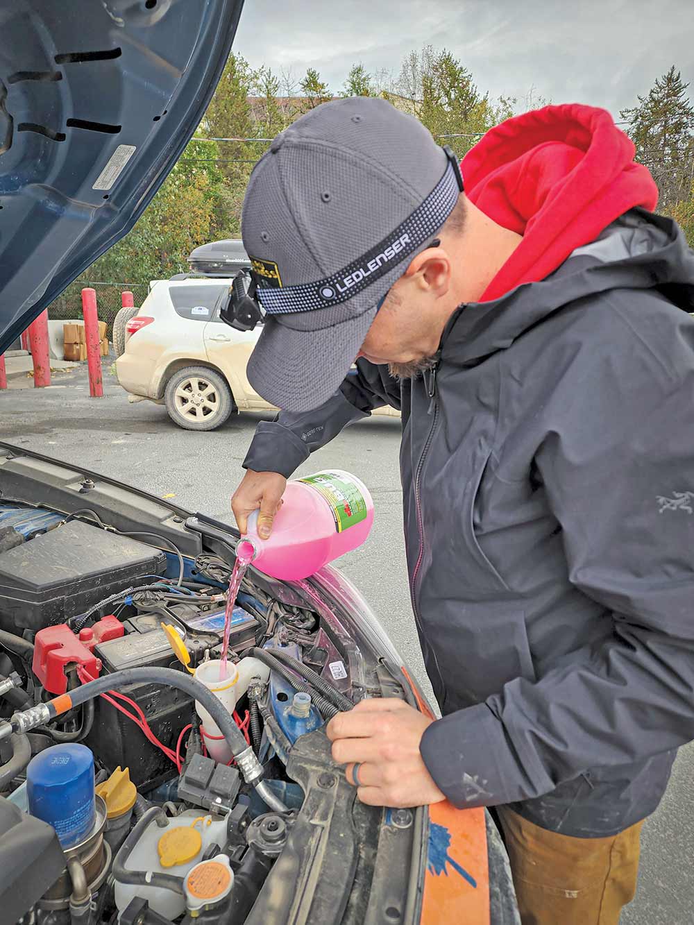 Male driver in a red hoodie and gray ballcap tops off fluids along the rally route.