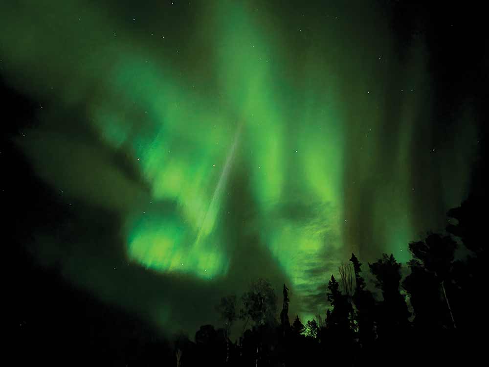 The northern lights flow green in the dark night sky. 