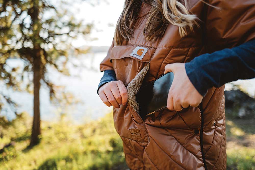 A woman tucks her phone into the sherpa pocket of this brown poncho coat.