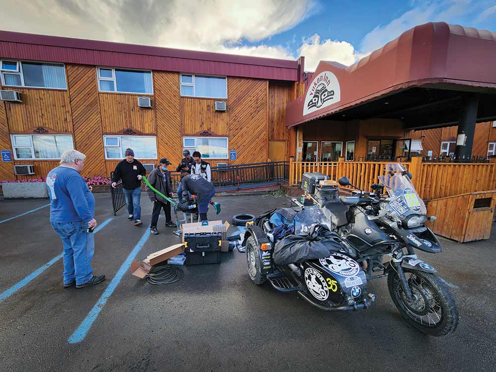 Parked at a roadside motel, an Alcan rally team stops to fix a flat tire.