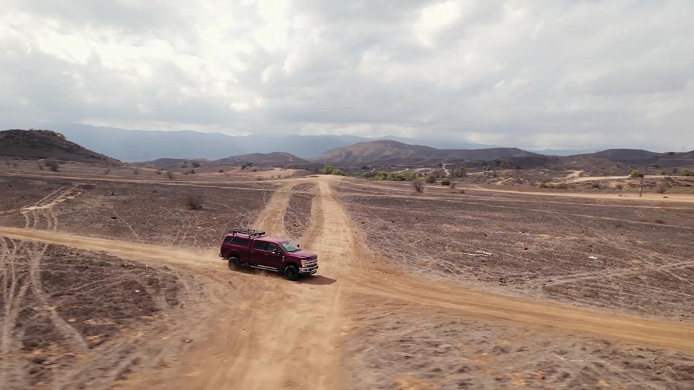 Drone shot of the red F250 making its way through an intersection of two light-colored tire paths in the desert.