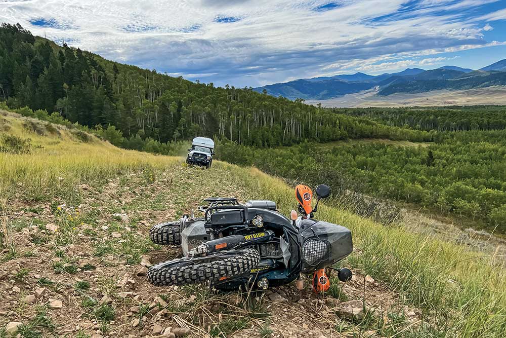 On a path through a grass field, a bike lies on its side. The support truck approaches, driving up the trail.