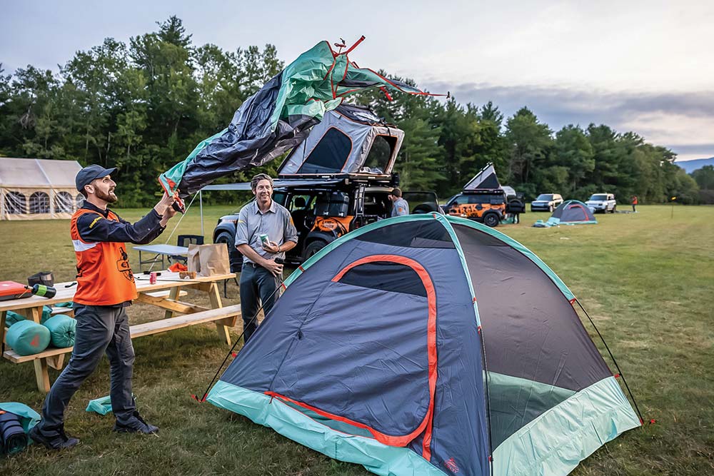 A man thows a rain fly over a gray and teal tent.