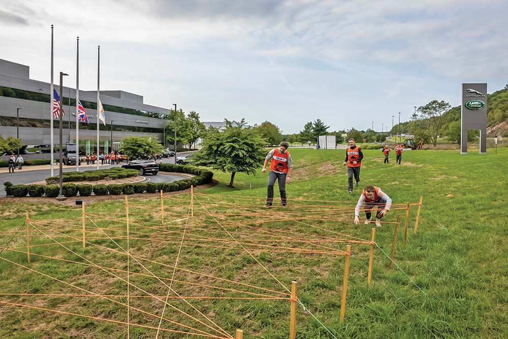 Several competitors begin to tackle a relay obstacle, a series of ropes arranged in a chaotic pattern that they must run through without touching.