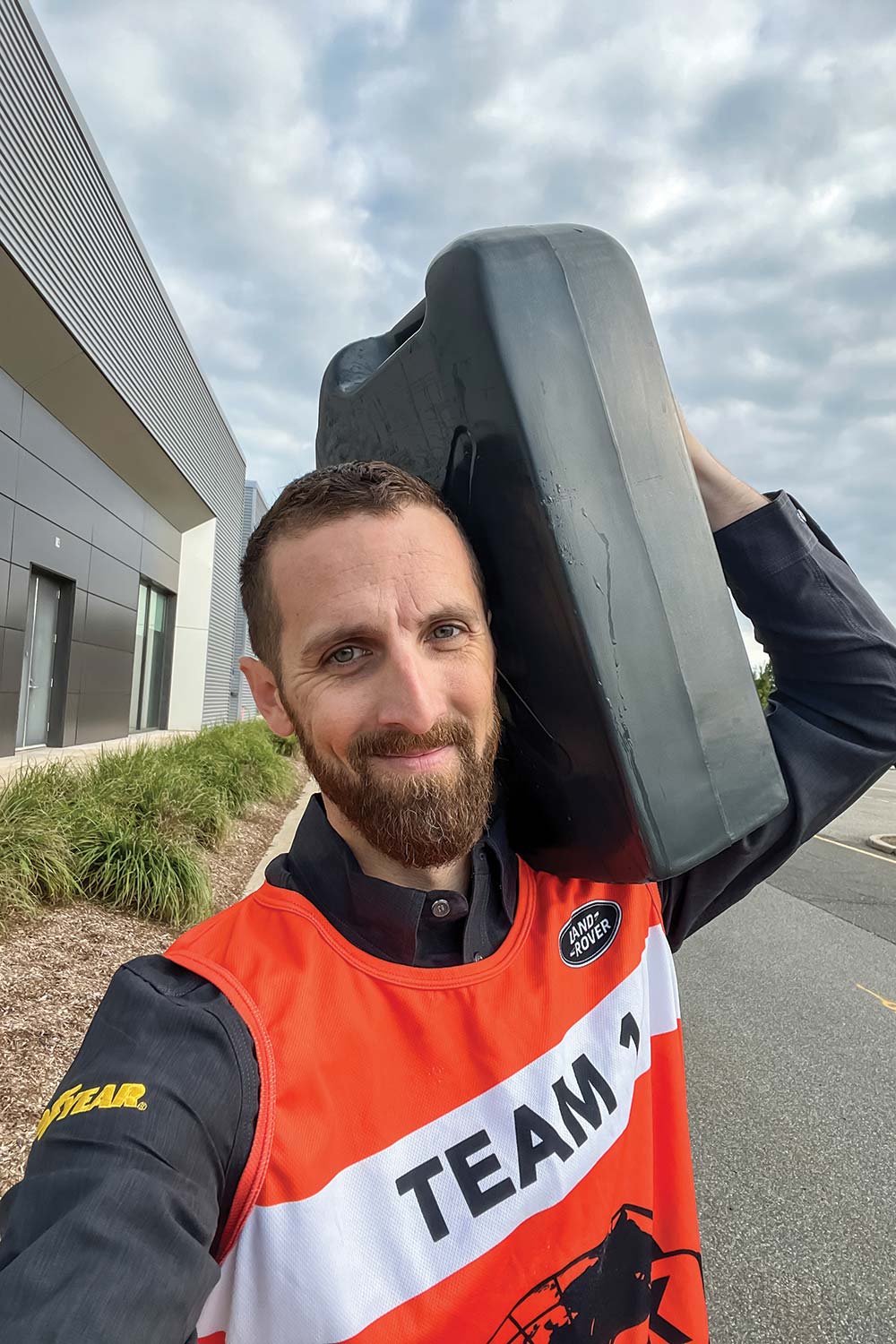 A selfie of the author, a bearded man, smiling while carrying a large black water jug on his shoulder.